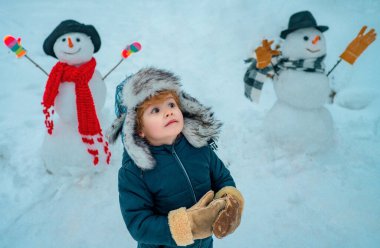 Kardan adam ve komik çocuk arkadaş kırmızı burunlu, kış şapkası ve eşarbıyla dikiliyor. Mutlu Noeller ve mutlu yıllar. Noel kışları çocuklar