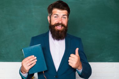 Erkek öğretmenin yakın plan portresi okulda kitabı kopya alanı olan tahtada tutuyor.