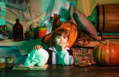 Cadılar Bayramı kostümü giymiş bir çocuk ve balkabağı eski ahşap bir ev. Cadılar Bayramı 'nız kutlu olsun tatlı çocuk balkabağıyla komik suratlar yapıyor. Cadılar Bayramı konsepti