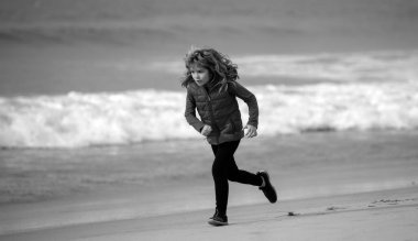 Deniz sahilinde koşan mutlu çocuk. Komik çocuk sörf kenarına doğru koşuyor. Aktif çocuk yaşam tarzı. Çocuklarla sabah koşusu