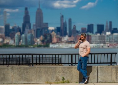 New York 'ta telefonla konuşan bir adam. New York Skyline 'da telefonla konuşan adam. Tişörtlü bir adam cep telefonuyla konuşuyor. Cep telefonuyla konuşan adam. Şehirdeki turistin elinde akıllı telefon var