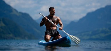 Kürek tahtası olan seksi adam. Kürek çeken bir adam. Sup board paddle sörfünde güçlü İspanyol adam. İsviçre 'deki Alps Gölü' nde yaz tatilinde SUP sörfü