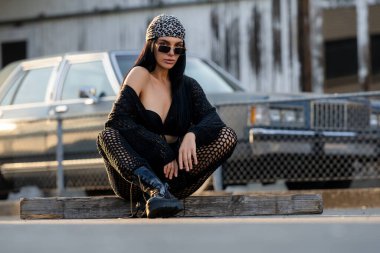 Rock tarzı seksi bir kadın sokakta kendine güvenerek poz veriyor. Cesaret ve cazibe saçıyor. Sinirli ve şık. Genç ve seksi hippi kadının moda portresi, siyah yaz tarzı kıyafetler giyiyor.