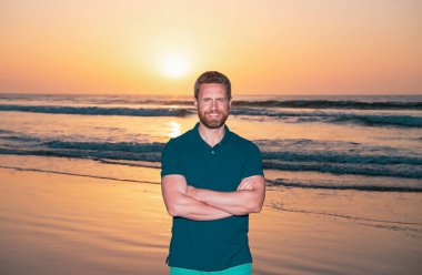 Tropik sahilde duran kaslı vücutlu, gülümseyen yakışıklı seksi adamın portresi. Yaz tatilleri. Güneşli bir günde, tropikal plajda poz veren yakışıklı bir adamın açık hava moda portresi.