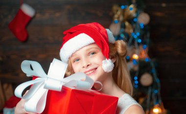Mutlu küçük kız kış giyim düşünüyorum hakkında Santa Noel ağacının yanında giymiş. Çocuk kapalı Noel ağacı yakınındaki eğleniyor