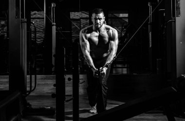 Güçlü kaslı adam spor salonundaki egzersizleri yukarı itiyor, trisepslerde egzersiz yapıyor. Spor yapan atletik erkek sporcu. Spor konsepti