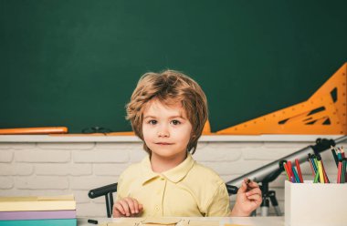 Komik yüzlü, sevimli bir öğrenci. İlkokul öğrencisi portresi kapalı alanda çalışıyor.