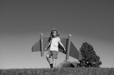 Küçük çocuk astronotu ya da pilotu oynuyor. Mavi gökyüzünün arka planındaki çocuk. Kağıt kanatlı çocuklar sırt roketi rüyası görür. Çocuklar uçmayı hayal eder. Oyuncak sırt roketli komik çocuk. Başarı, hayal gücü