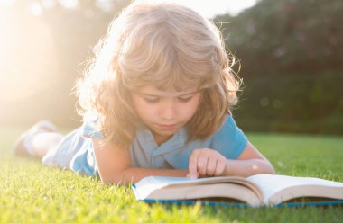 Küçük çocuk yaz gün batımında kitap okuyor.