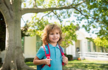 Child with rucksacks standing in the park near school. Pupils with books and backpacks outdoors. Kids education concept clipart