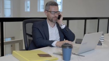 Ofis çalışanı telefonda dizüstü bilgisayarla konuşuyor. İş adamının ofiste telefon görüşmesi var. Modern ofiste iş adamı telefonda konuşuyor. Telefon kullanan bir iş adamı. İş konuşması