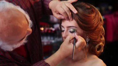 Makyaj sanatçısı güzellik makyajı modeli için göz farı sürüyor. Yakından bak, göz farı. Moda gözlüklü güzel bir genç kadın. Kozmetik. Mükemmel bir göz farı ve güzellik makyajı.