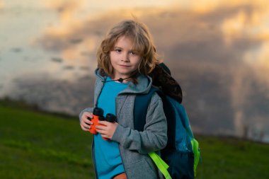 Keşiflerin rüyaları. Dürbünle oynayan mutlu çocuk. Keşif ve macera. Sırt çantalı çocuk doğayı ve çevreyi keşfediyor. Çocuklar için açık hava eğlence etkinliği