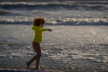 Çocuk yaz denizinde oynuyor. Çocuklar tropikal tatil köylerinde oynarlar. Denizde koşan bir çocuk. Yüzme, yaz tatili. Çocuk deniz suyunda oynuyor. Çocuk deniz suyunda yaz tatilinin tadını çıkarıyor.