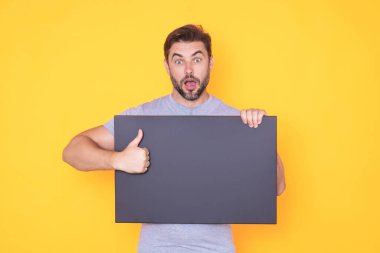 Boş tahtayı tutan ve tekneyi işaret eden yakışıklı bir adam. Telif uzayı olan boş bir tahta gösteriyor. Fikir ve teklif. Reklamınız. Metin ve maket için boş alanı olan boş reklam panosu