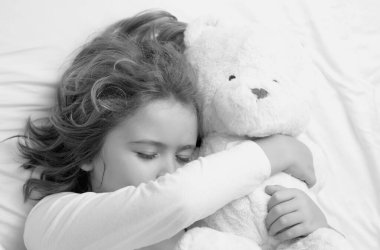 Günlük uyku. Oyuncak ayıyla yatakta uyuyan bir çocuk. Battaniyenin altında uyuyan tatlı çocuk. Çocuk yastığa uzanmış. Çocuk uyuyor, sağlıklı bir uyku çekiyor ya da kestiriyor.