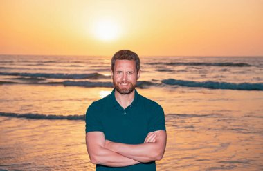 Deniz manzarasında poz veren tişört giyen yakışıklı bir adam..