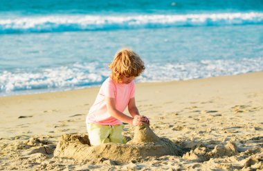 Çocuk yaz tatilinde plajda oynuyor. Çocuklar denizde kumdan kale yapıyorlar.