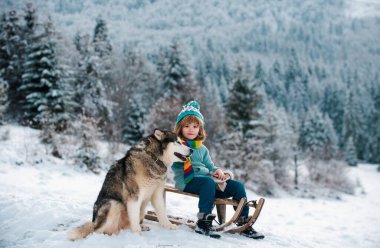 Köpek gibi köpekleri olan çocuklar için açık hava oyunları. Mutlu Noel tatili konsepti. Çocuk kışın tadını çıkarıyor, kış ormanlarında kızak gezintisiyle oynuyor.