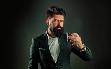 Siyah takım elbiseli, çatı katında viski bardağı olan kendine güvenen sakallı adam. Camdan alkol içen adam