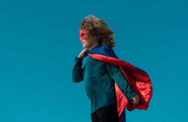 Süper kahraman kostümü giyen bir çocuk. Mavi yaz gökyüzü geçmişine karşı süper kahraman çocuk. Çocuk dışarıda eğleniyor. Çocukların güç konsepti