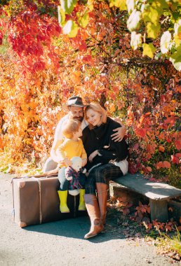 Küçük çocuk bavulun üzerine oturmuş hippi ailesiyle konuşuyor. Atmosferik muhteşem aile fotoğrafı. Burgundy sonbahar yaprakları arka planı. Güneşli ve ılık sonbahar günü rahatla. Aile kavramı