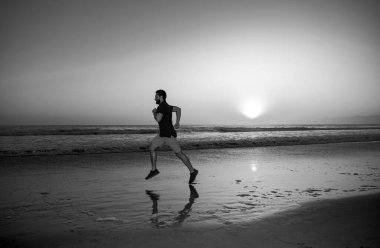 Günbatımında tropik plajda koşan bir adam. Sağlıklı bir adamın koşması ve dışarıda koşması. Erkek koşucu. Spor ve sağlıklı yaşam tarzı