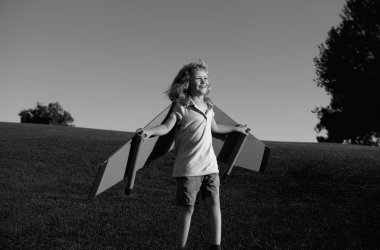 Çocuk yaz parkında oyuncak uçak kanatlarıyla oynuyor. Yenilik teknolojisi ve başarı konsepti. Çocuk pilot parkta çimlerde eğleniyor. Mutlu çocuk dışarıda oynuyor.