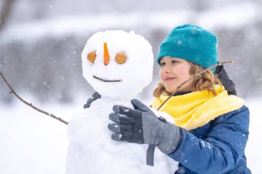 Soğuk bir kış gününde, kış parkında mutlu çocuk. Kışın karla oynayan sevimli bir çocuk. Kardan adamla komik çocuk portresi. Noel 'de kış aktiviteleri. Parkta kardan adam yapan çocuk