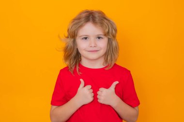 Stüdyonun izole edilmiş arka planında onayını veren sevimli bir çocuk. Çocuk portresi başparmak işareti yapıyor.