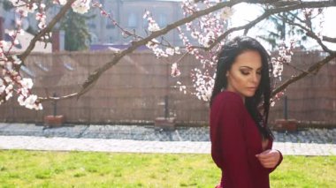 Genç ve güzel bir kadın çiçek parkında poz veriyor. Bahar çiçeğinin yanında tasasız bir model. Bahar parkında, pembe çiçeklerin yanında güzel bir genç kız. Bahar doğasında şefkatli romantik model