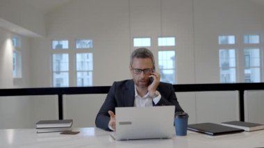 Ofis çalışanı telefonda dizüstü bilgisayarla konuşuyor. İş adamının ofiste telefon görüşmesi var. Modern ofiste iş adamı telefonda konuşuyor. Telefon kullanan bir iş adamı. İş konuşması