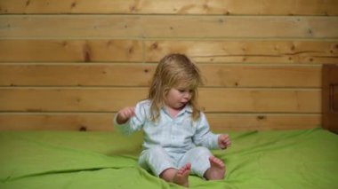 Pijamalı bebek gülüyor ve eve yatağa atlıyor. Çocukluk, günaydın. Bebek yatakta zıplıyor, evde eğleniyor. Çocuk zıplayarak ve yatakta oynayarak eğleniyor. Yatak odasında bebek oyunu