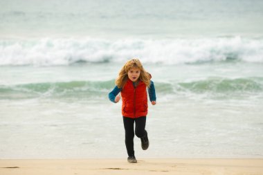 Mutlu çocuk denize koşuyor. Çocuk sahilde eğleniyor, deniz havuzu işletiyor. Aktif aile hayatı, çocuklar açık deniz sporları. Çocuklarla sabah koşusu