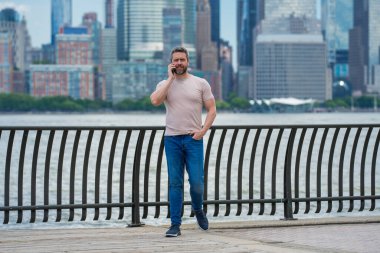 New York 'ta telefonla konuşan bir adam. İspanyol adam telefonda konuşuyordu. Tişörtlü adam cep telefonuyla konuşuyor. Cep telefonuyla konuşan adam. Şehirdeki turistin elinde akıllı telefon var