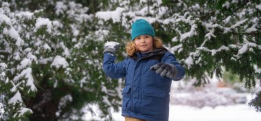 Çocuk kış parkında karla oynuyor. İlk karlı kış çocukları. Çocuk kış tatili. Kış parkında karla oynayan gülümseyen çocuk. Örgü şapkalı küçük bir çocuğun portresi. Kar topu atıyor. Komik kar