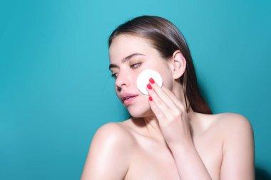 Removing makeup with cotton pads. Cleaning face with pad. Cosmetic cotton pad. Young woman caring for facial skin using cotton pad in studio. Beauty care and pampering. Daily skincare