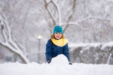 Heyecanlı Çocuk kışın kardan adam için kartopu yapıyor. Çocuk karda oynuyor. Açık havada aktif kış oyunları. Çocuk karla oynarken eğleniyor. Çocuklar için açık havada kış tatili. Güneşli kış gününde çocuk oyunu