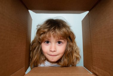 Kid boy unpacking and opening carton box looking inside with surprise face. Children expression surprised face