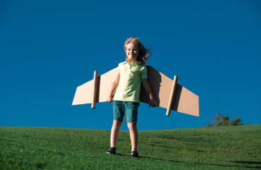 Çocuk parkta karton oyuncak kanatlarla oynuyor. Çocuk günü kavramı. Pilot kostümlü çocuk oynuyor ve havacı uzay adamı olmanın hayalini kuruyor.