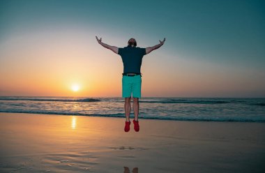 Kaygısız adam plajda zıplıyor, gün batımında siluet