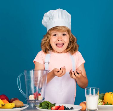 Heyecanlı komik aşçı. Aşçı şapkalı şefin portresi. Evde yemek pişiren, sebze ve meyvelerden yemek hazırlayan çocuk. Sağlıklı beslenme