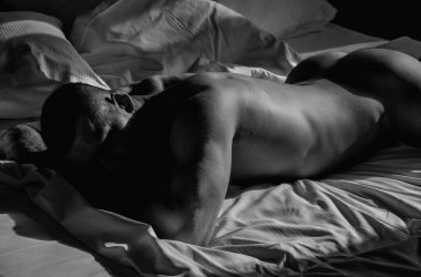 Seductive gay. Muscular body of man in bed. Strong brutal guy. Sexy male naked torso. Nude muscular body man with tattoo lay in the bed. Muscular laying on bed. Sexy back