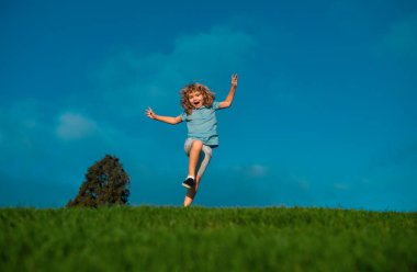 Little adorable boy running on grass. Excited kid play the green grass. The child has blond long hair and a t-shit. The concept of harmony with nature and care for ecology. Healthy lifestyle