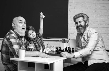 Grandfather father and son playing chess, happy men generations family. Old grandfather and cute little boy grandson study and learn together. Senior grandpa and middle aged dad play playing chess