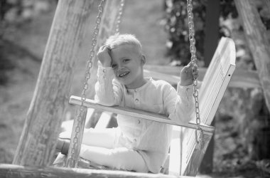 Çocuk salıncakta oynuyor. Sıcak havalarda çocuklar için sağlıklı bir yaz etkinliği. Küçük çocuklar sallanıyor. Güzel bir yaz bahçesinde salıncakta sallanan sevimli küçük bir çocuk. Çocukluk, yaz tatili