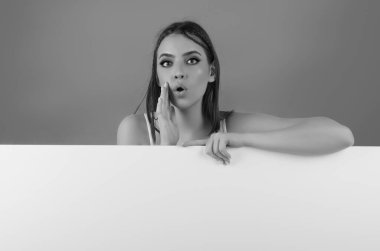 Stüdyo arka planında boş bir ilan panosu tutan kadın. Neşeli şirin kız beyaz boş afişin arkasında duruyor, kopyalama alanı. Boş tahta var. Boş tahtası olan stüdyo kadın portresi