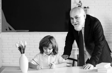 School boy grandson reading book and writing with old senior teacher grandfather