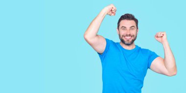 Kazanan. Başarılı bir adam kollarını kaldırdı. Kollarını kaldırıp başarıyı kutlayan heyecanlı adam. Mavi arka planda izole edilmiş heyecanlı bir erkek modelin portresi. Kutlama yapan adam kazanır. Başarı. Heyecanlı kazanan