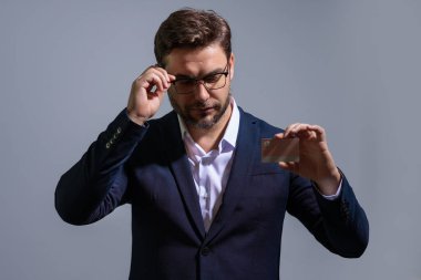Elinde kredi kartı tutan yakışıklı bir adam. Gri stüdyo geçmişinde kredi kartı olan orta yaşlı bir adam. Kredi kartı konsepti. Takım elbiseli bir işadamı kredi kartıyla ödeme yapıyor.